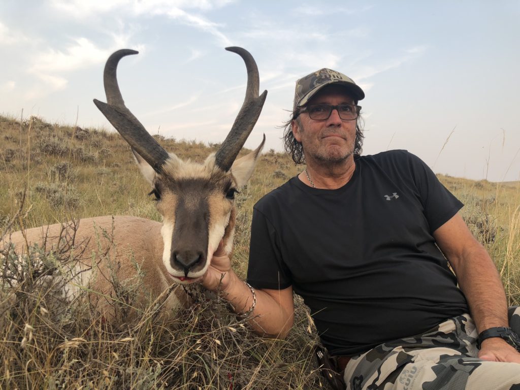 A man wearing glasses and camouflage hat sitting next to and holding his trophy antelope after an antelope guided hunt