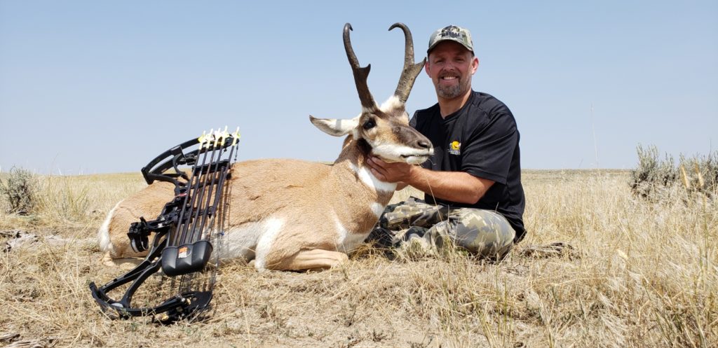 Man with a goatee wearing camouflage hat sitting next to and holding his trophy antelope