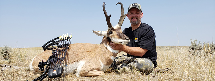 Bow hunter smiling with his bow resting against the Antelope he caught